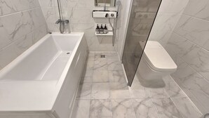 A bathroom with a bathtub, toilet, and shower area, featuring marble tiles and a glass shower enclosure. - Suwon Station Hotel Terry's (Suwon)