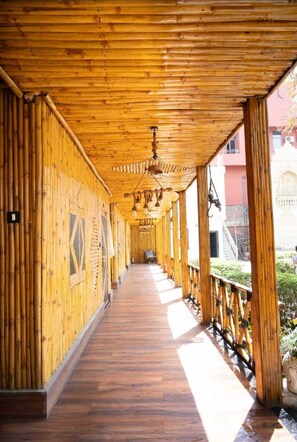 A covered wooden corridor with a wooden floor, a hanging light fixture, and a railing on one side. - First Impression (Varanasi)