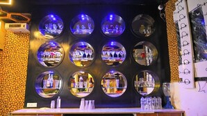 A bar area with circular mirrors, a wooden wall, and a counter with bottles and glasses. - First Impression (Varanasi)