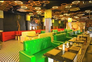 A restaurant with green and red seating, a patterned floor, and a ceiling with geometric light fixtures. - First Impression (Varanasi)