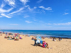 A beach with people sunbathing and swimming, and a clear blue sky. - Torreblanca near the sea (Torrevieja)