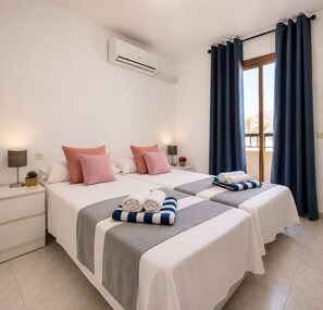 A hotel room with two beds, a window with curtains, an air conditioning unit, and a small plant on the nightstand. - Torreblanca near the sea (Torrevieja)