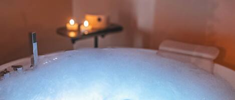 A hot tub with a wooden edge, a small table with candles, and a wall in the background.