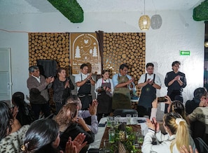 A group of people clapping in a room with a patterned wall and a sign with text.