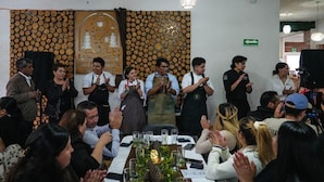 A group of people clapping in a room with a wall decorated with circular patterns and a logo.