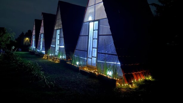 A row of modern, triangular-shaped buildings with large windows, illuminated by internal lighting.