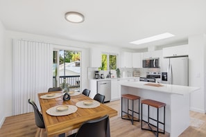 A modern kitchen with white cabinetry, a central island with stools, a dining table with placemats, and a view of the outdoors.