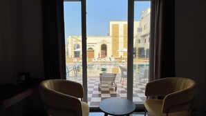 A room with two chairs, a small table, and a view of an outdoor pool area. - VRINDA HOTELS (Sitapur)