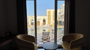 A room with two chairs and a small table, large windows with a view of buildings and a pool. - VRINDA HOTELS (Sitapur)