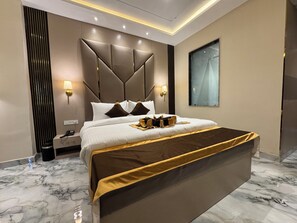 A modern hotel room with a large bed, a bedside table with a phone, a wall-mounted lamp, and a window with a view. - VRINDA HOTELS (Sitapur)