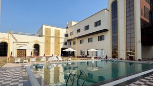 A swimming pool with checkered flooring, lounge chairs, and a building with a checkered facade. - VRINDA HOTELS (Sitapur)