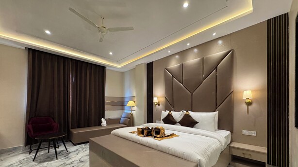 A modern hotel room with a large bed, a bedside table, a chair, and a ceiling fan. - VRINDA HOTELS (Sitapur)