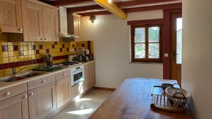 A kitchen with wooden cabinets, a tiled backsplash, a window, and a wooden table with a basket. - A 75 m² self-contained vacation rental surrounded by nature, fully equipped with all modern comforts, for 2 people (Saou)