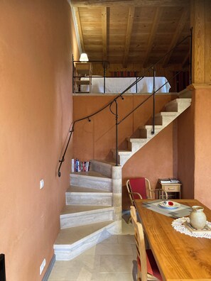A staircase with a metal railing leading to an upper level, a dining table with a vase and books, and a chair.