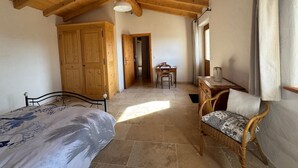 A room with a wooden ceiling, a bed with a floral bedspread, a wicker chair with a patterned cushion, a wooden table with a pitcher, and a wooden wardrobe. - A 75 m² self-contained vacation rental surrounded by nature, fully equipped with all modern comforts, for 2 people (Saou)