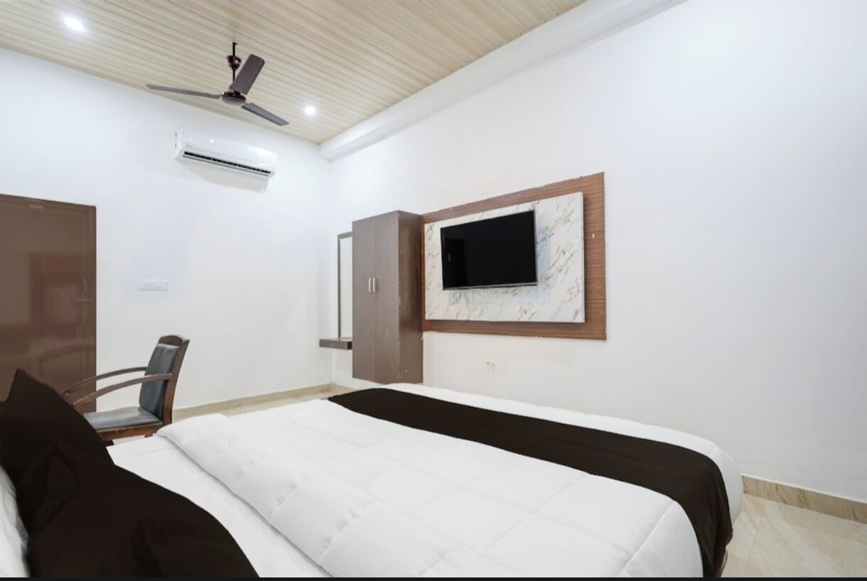 A bedroom with a bed, a TV mounted on the wall, a ceiling fan, and an air conditioning unit.