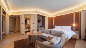 A hotel room with a bed, a sofa, a small table, a chair, a round mirror, and a wall-mounted light fixture. - Orange Crystal Hotel Yangjiang (Yangjiang)