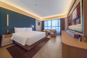 Quarto de hotel com uma cama grande, uma escrivaninha, uma cadeira, uma televisão e uma janela com cortinas.