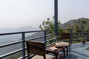 A balcony with a wooden table, chairs, and a view of a mountainous landscape.