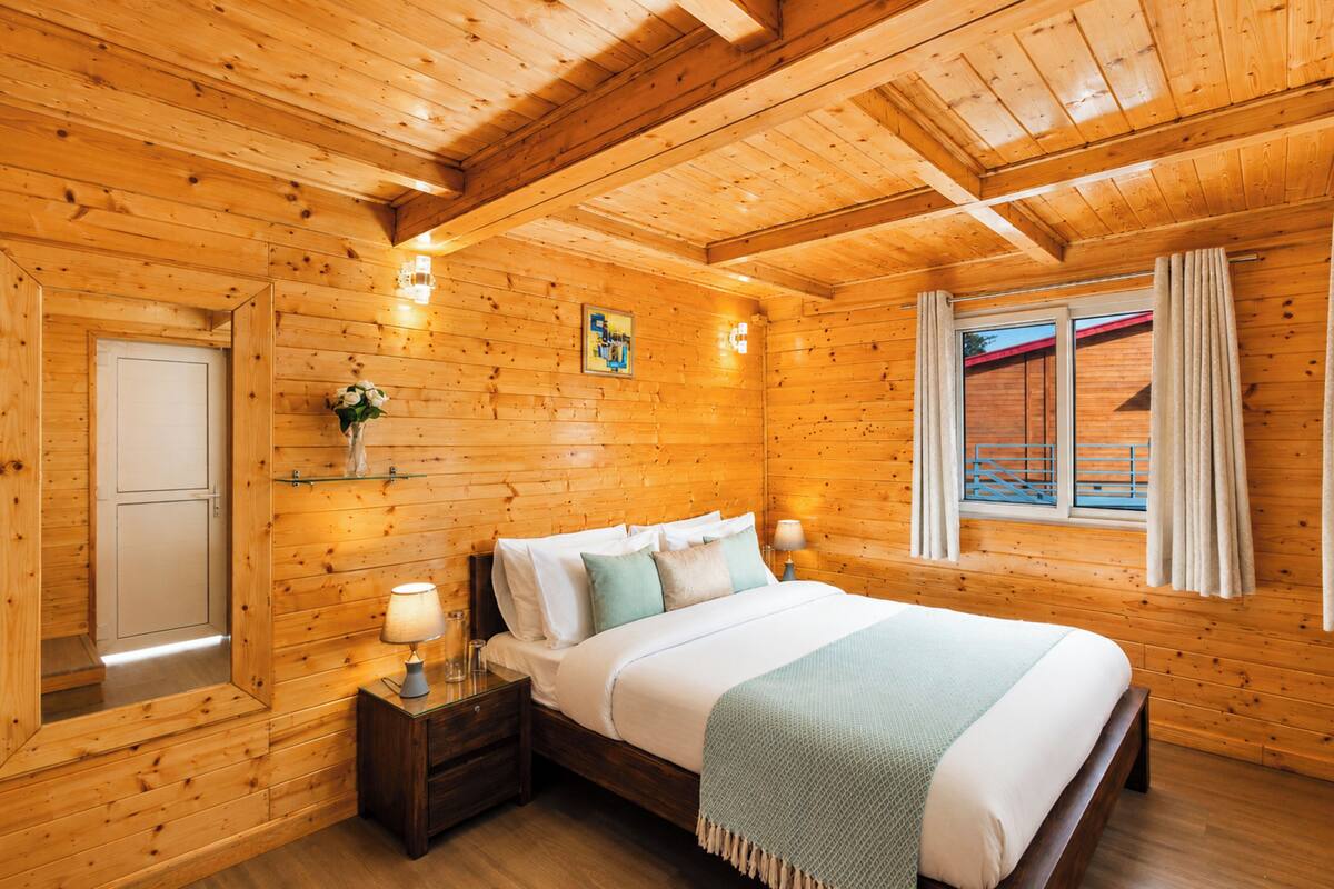 A wooden cabin bedroom with a bed, nightstands, a window with curtains, and a wooden ceiling.