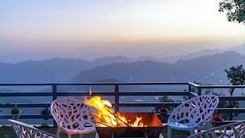 A fire pit with chairs, a railing, and a mountainous backdrop.