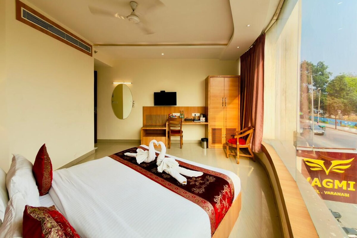 A hotel room with a bed, a desk, a chair, a television, and a view of the outside.