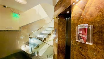 Un interior de hotel moderno con una escalera de cristal, paredes de mármol y un atril con revistas.