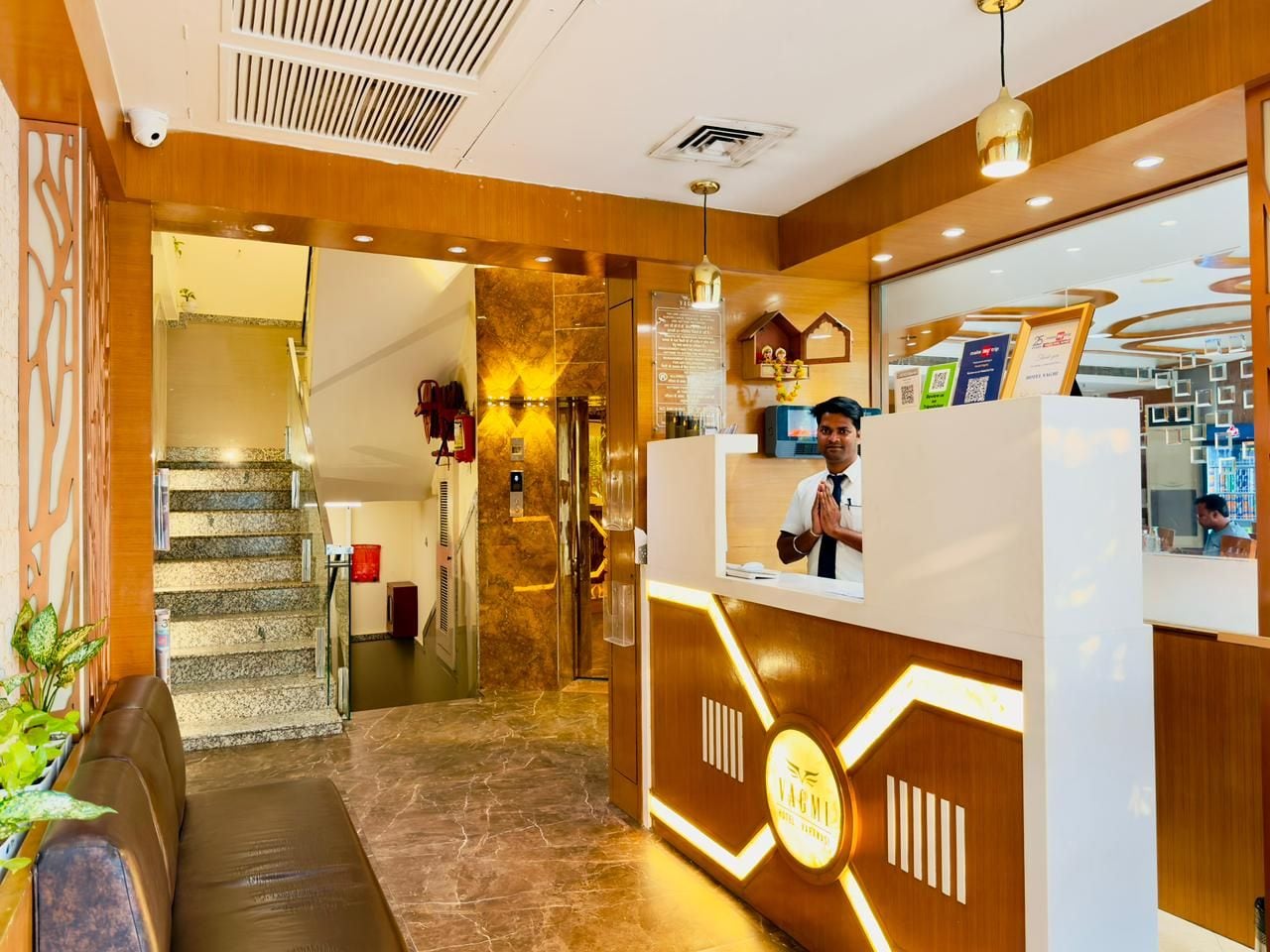 Zona de recepción de hotel con mostrador, escalera y área de descanso.