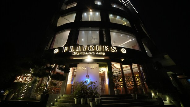 Um edifício de vários andares com um restaurante chamado 'FLAVOURS' no nível térreo.