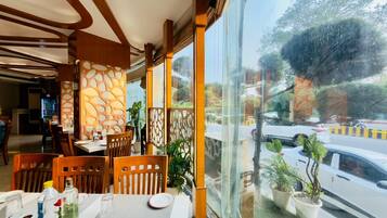 A restaurant with a view of the street, wooden furniture, and potted plants.