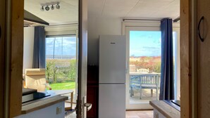 Une cuisine compacte équipée d’un réfrigérateur, un coin repas avec une table et des chaises, et une vue sur l’extérieur.