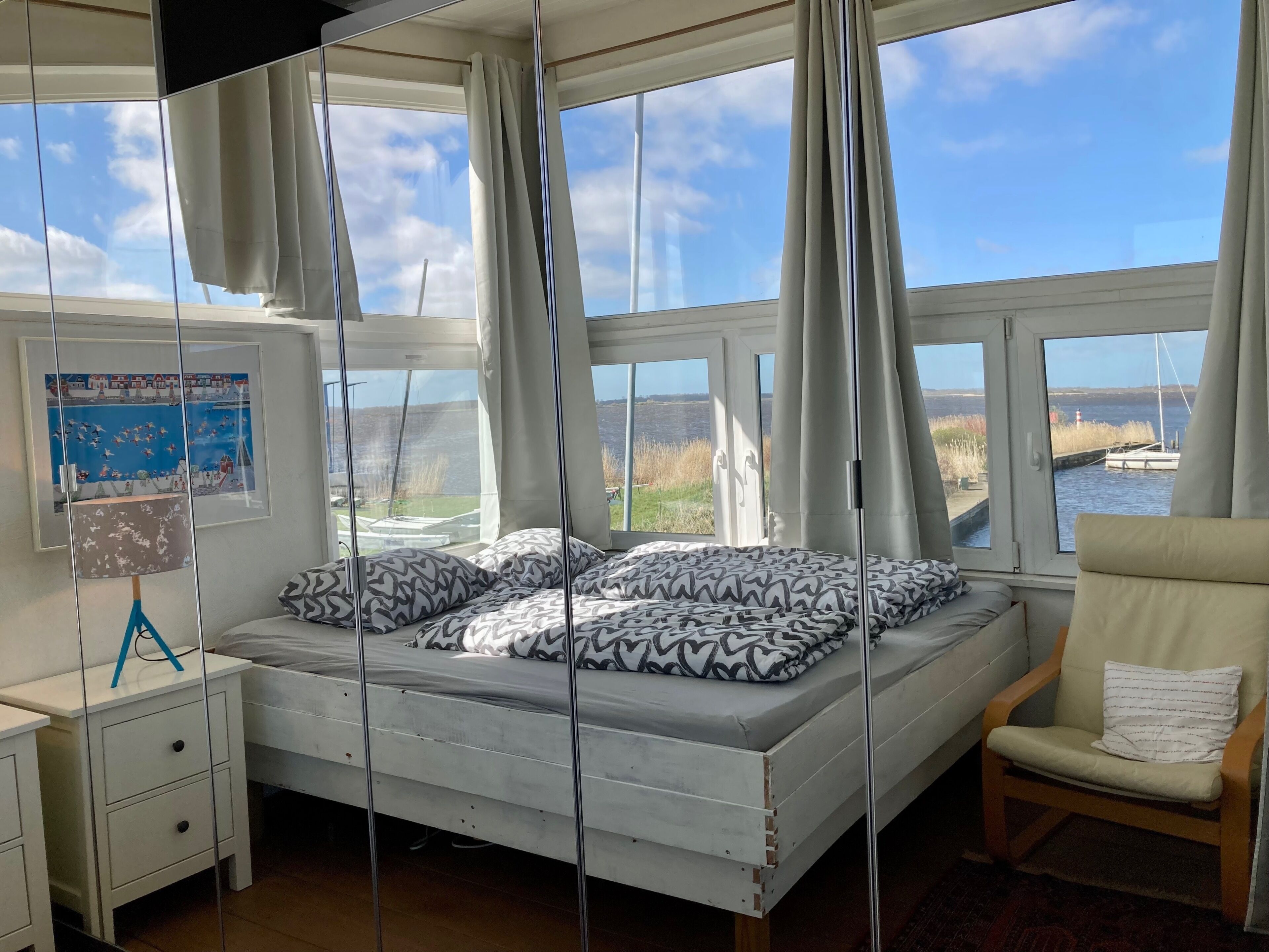 A bedroom with a bed, a chair, a desk, and large windows with curtains.