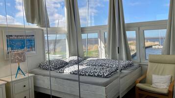 A bedroom with a bed, a chair, a desk, and large windows with curtains.