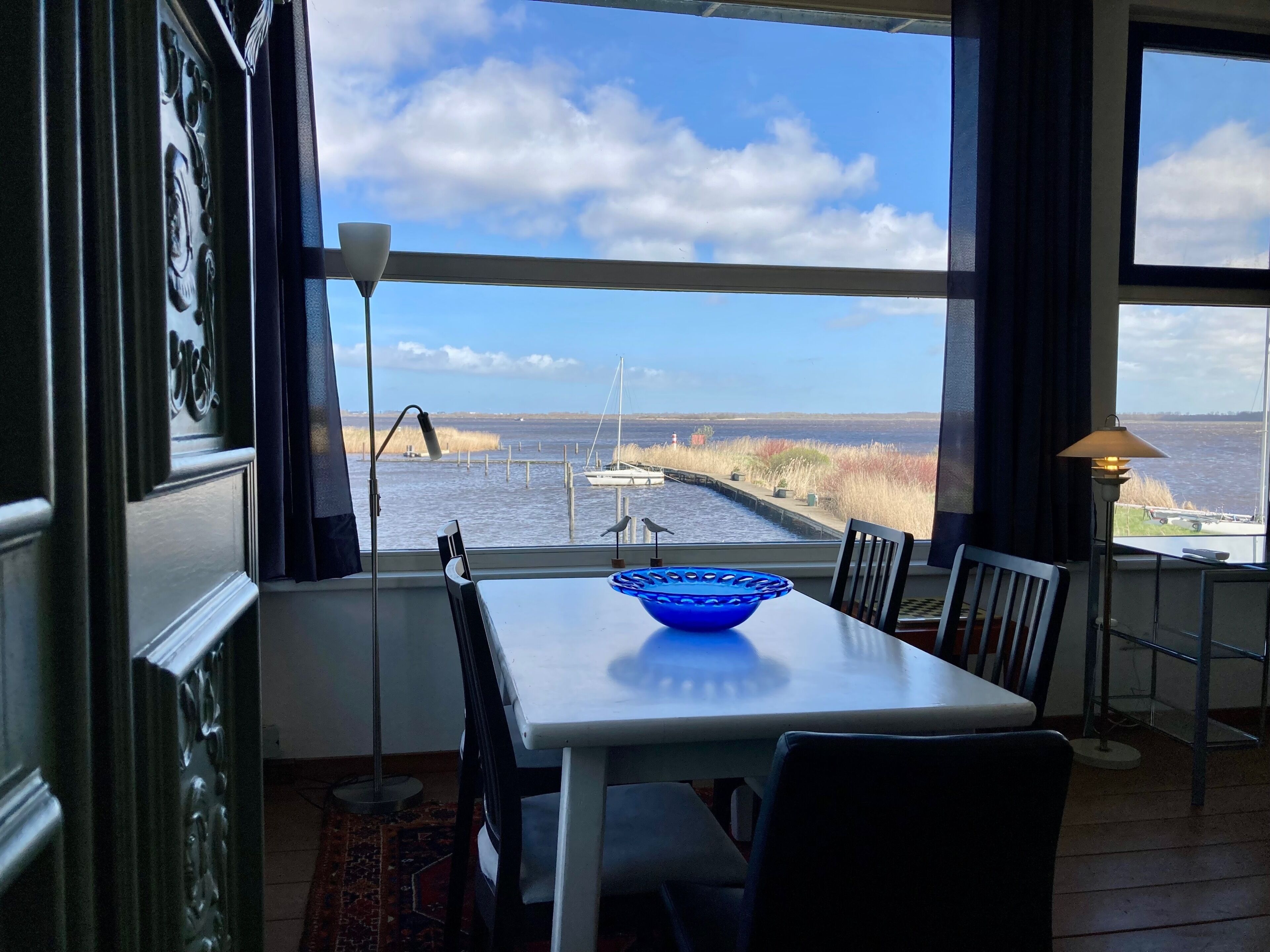 A dining area with a table, chairs, and a view of a body of water with boats.