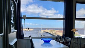 Un espace repas comprenant une table, des chaises et donnant sur un plan d’eau où se trouvent des bateaux.