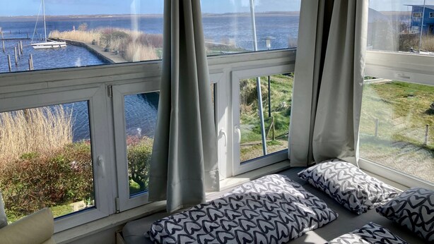 Une chambre dotée d’une grande fenêtre donnant sur un plan d’eau, d’un lit agrémenté d’oreillers à motifs et offrant une vue sur un quai où sont amarrés des bateaux.