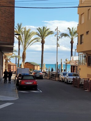 A street with parked cars, palm trees, and buildings. - A beautiful beachfront flat for 4 people with a lovely terrace overlooking sea (Torrevieja)
