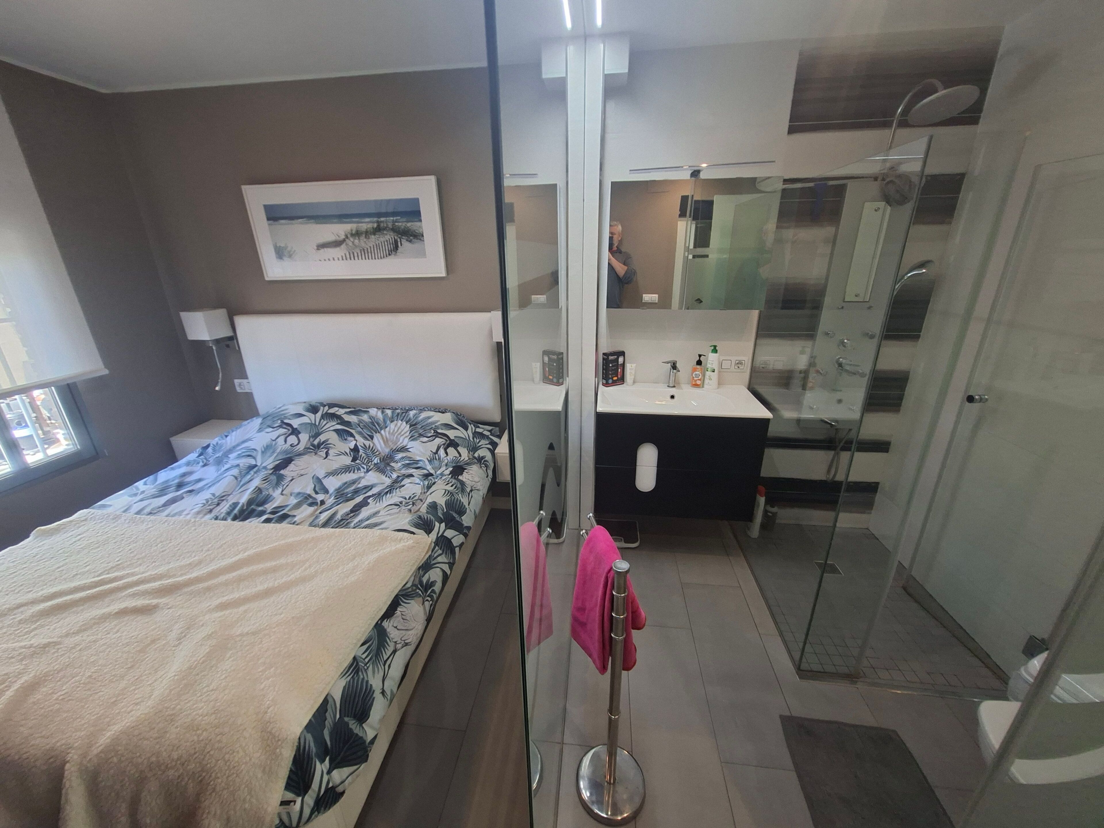 A hotel room with a bed, a bathroom with a sink, mirror, and shower.