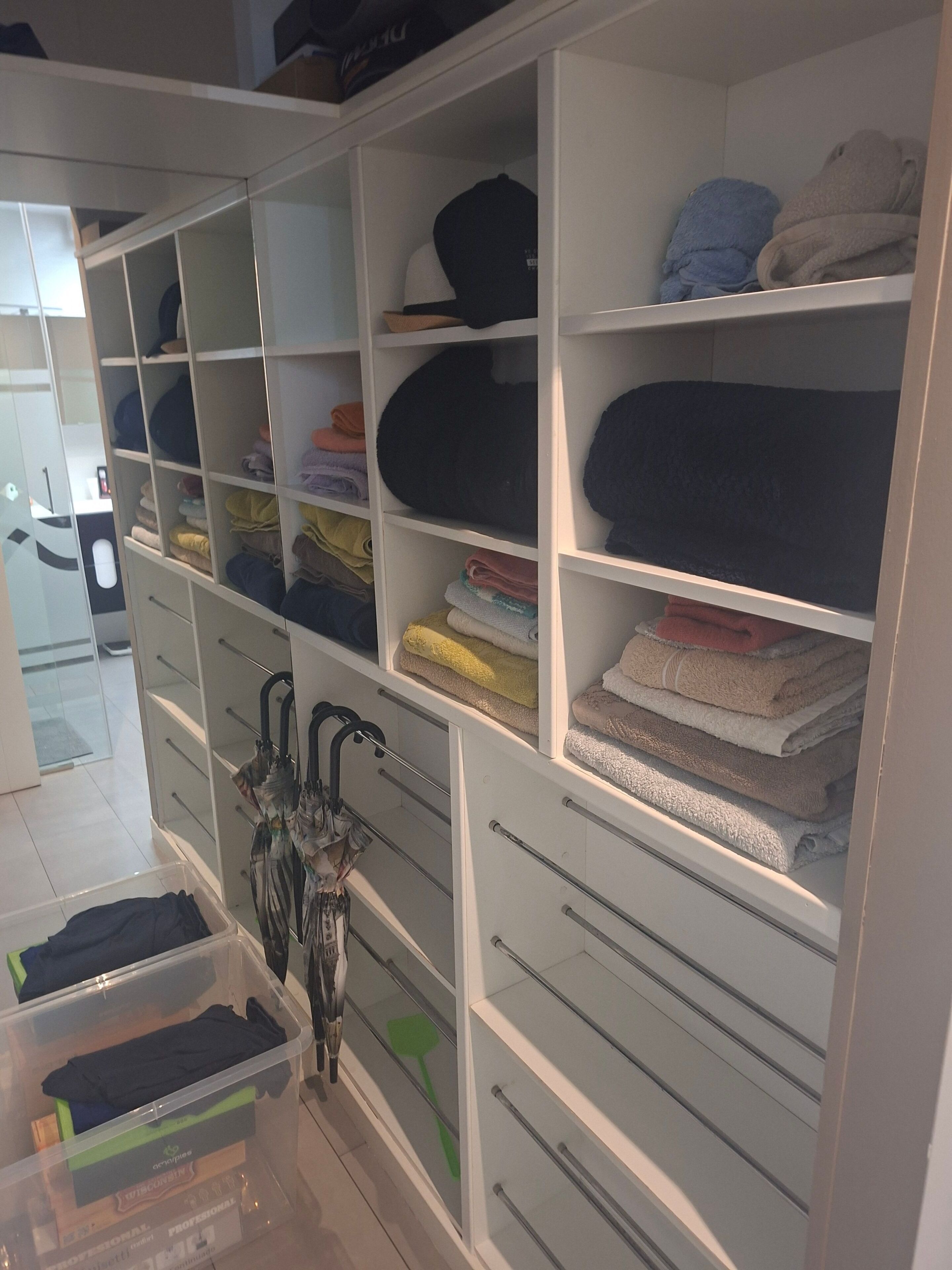 A well-organized closet with multiple shelves and drawers, containing neatly folded clothes and accessories.