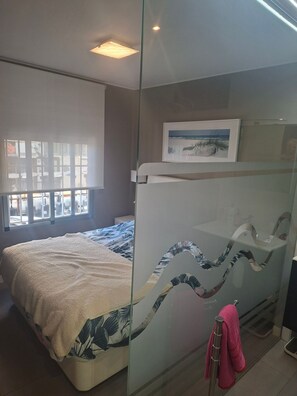 A bedroom with a bed, a glass partition, a framed picture, and a window with blinds. - A beautiful beachfront flat for 4 people with a lovely terrace overlooking sea (Torrevieja)