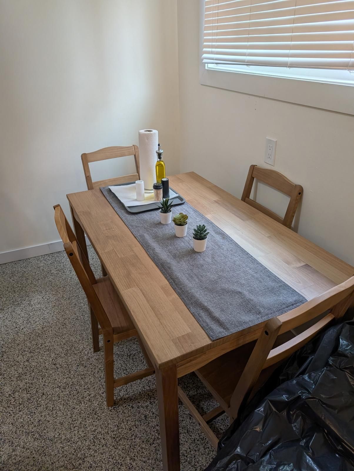 Une table à manger avec un set de table gris, deux petites plantes en pot, une bouteille et un rouleau d’essuie-tout.