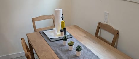 Una mesa de comedor con un posavasos gris, dos pequeñas macetas con plantas, una botella y un rollo de toallas de papel.