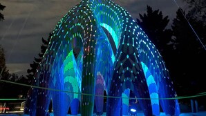 Een grote, verlichte koepelstructuur met een symmetrisch ontwerp, ondersteund door meerdere pilaren.