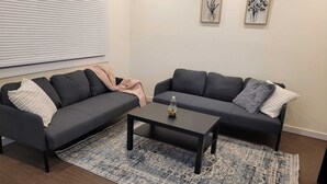 Een woonkamer met twee donkere banken, een salontafel, een kamerkleed met patroon en twee ingelijste kunstwerken aan de muur.
