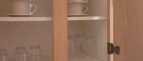 Una cocina con armarios de madera, un tostador y vasos de vidrio transparentes en los estantes.