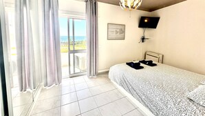 A bedroom with a bed, a TV, a view of the ocean, and a balcony with curtains. - Max Crib Sea View Apart with AC and Garage (Armação de Pêra)
