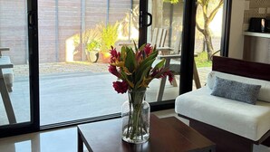 A modern living room with a sofa, a coffee table with a vase of flowers, and a sliding glass door leading to an outdoor area. - CASA RAMONA COSTA RICA (Santa Cruz)