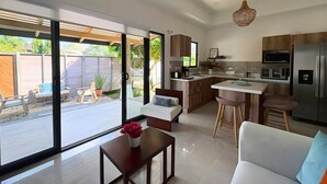 A modern kitchen with a central island, a dining area with a white table and chairs, and a living room with a sofa and a coffee table. - CASA RAMONA COSTA RICA (Santa Cruz)