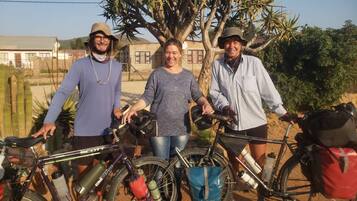 Three people standing with bicycles, a tree, and a building in the background.