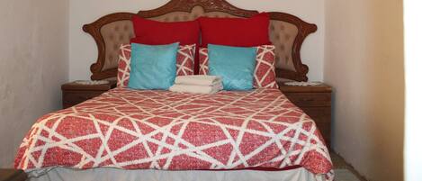 A bed with a geometric patterned bedspread, two red pillows, and two blue pillows. There are three wall art pieces above the bed.
